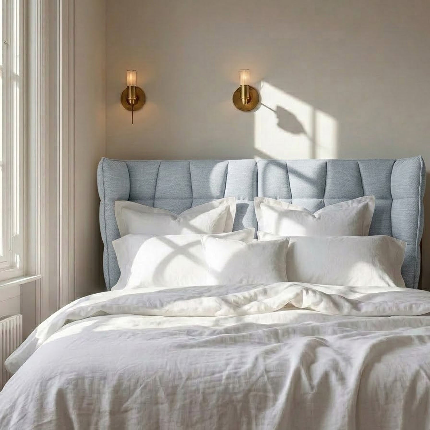 A contemporary bedroom featuring the Dortmund upholstered storage bed with a light blue tufted headboard, white linens, and sunlight casting a window shadow on the beige wall.