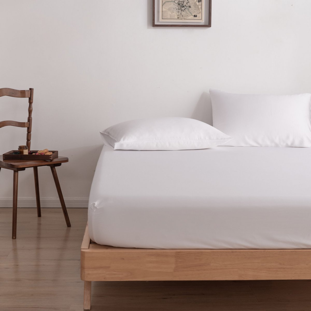 Coco White bamboo fitted sheet on a bed beside a wooden chair with a breakfast tray.