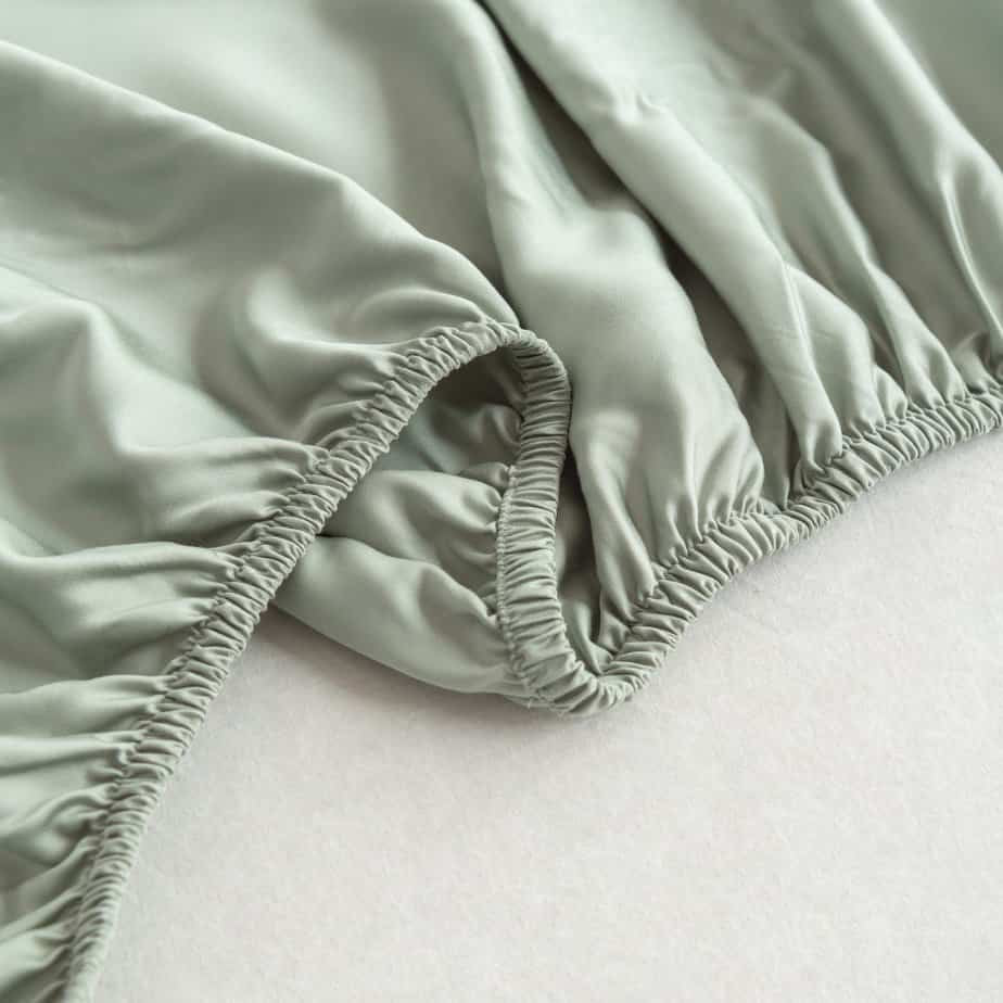 Close-up of the Sage Green bamboo fitted sheet's folded elastic corner off the mattress.