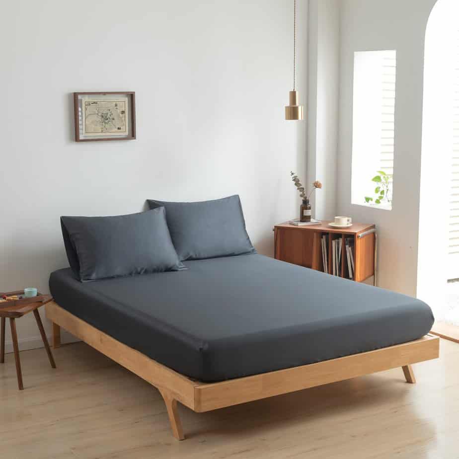 Space Blue bamboo fitted sheet styled on a wood-frame bed in a bright bedroom.