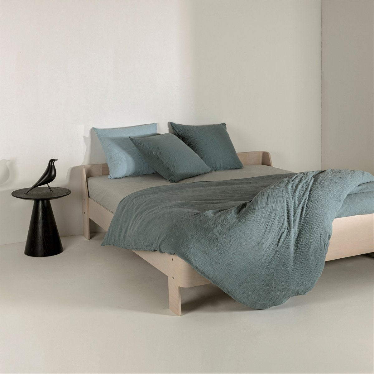 Petrol blue cotton muslin duvet cover with light blue pillowcases styled on a wooden bed frame