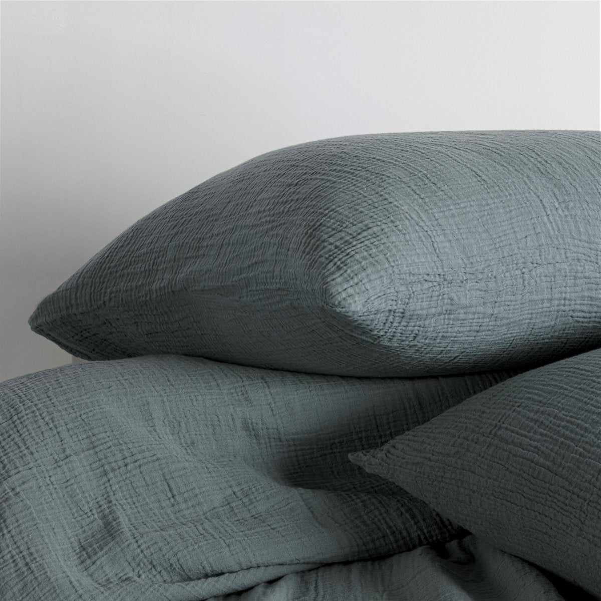Close-up of petrol blue cotton muslin pillows showing the wrinkled fabric texture