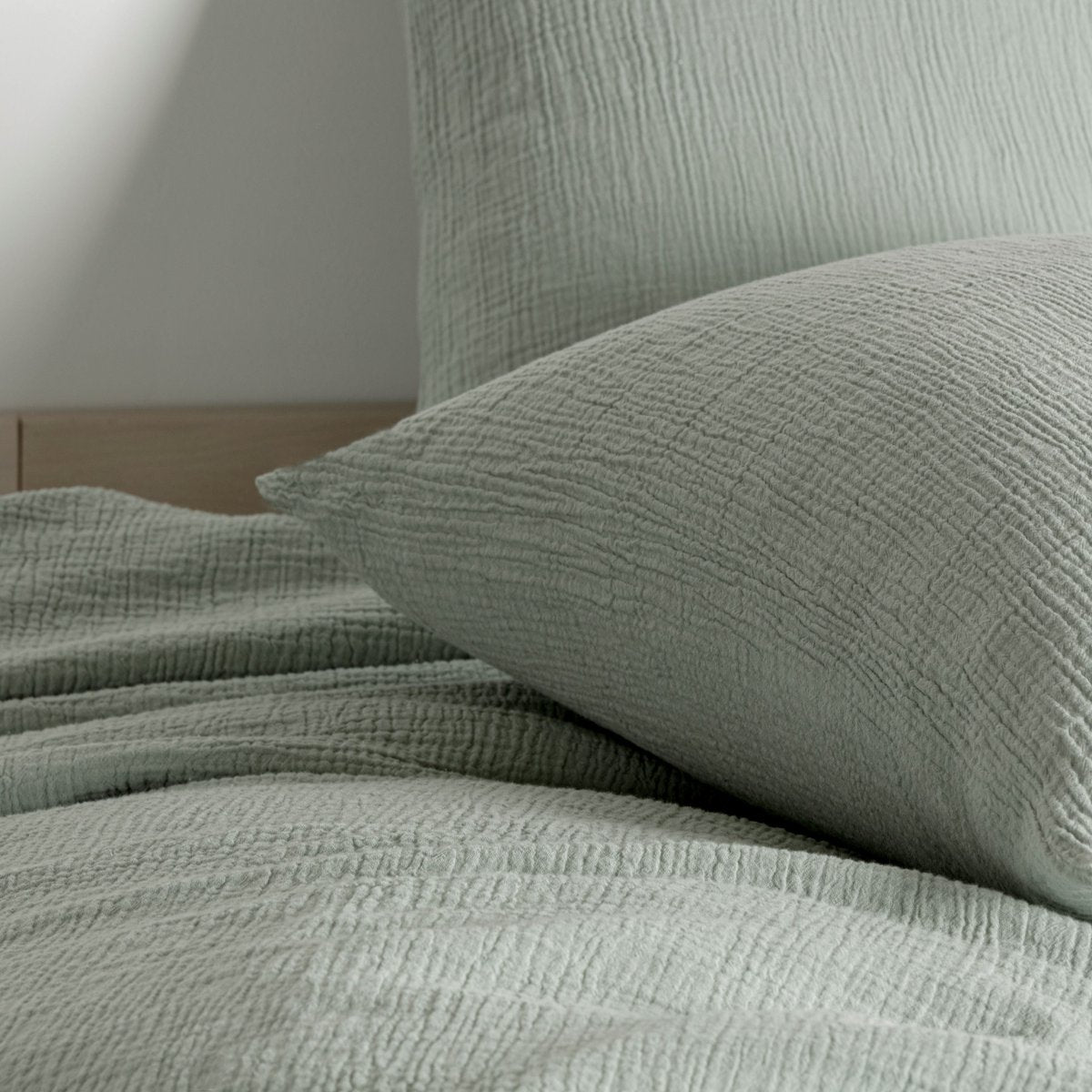Close-up of sage green cotton muslin pillow and duvet cover showing the wrinkled texture