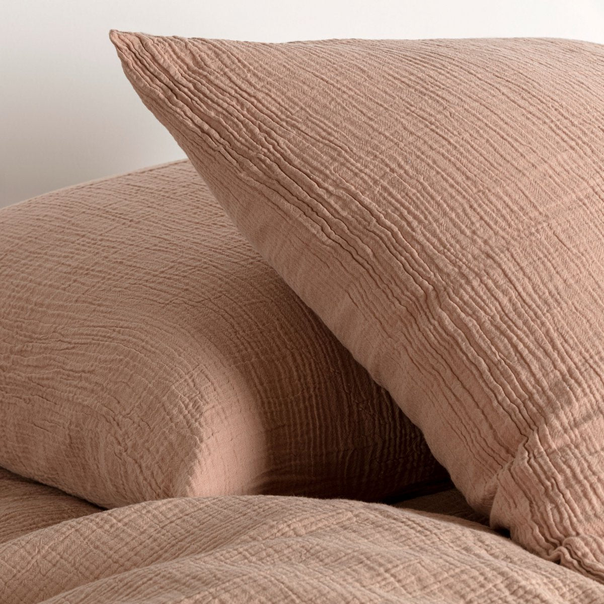 Close-up of sahara pink cotton muslin pillowcases showing the wrinkled fabric texture