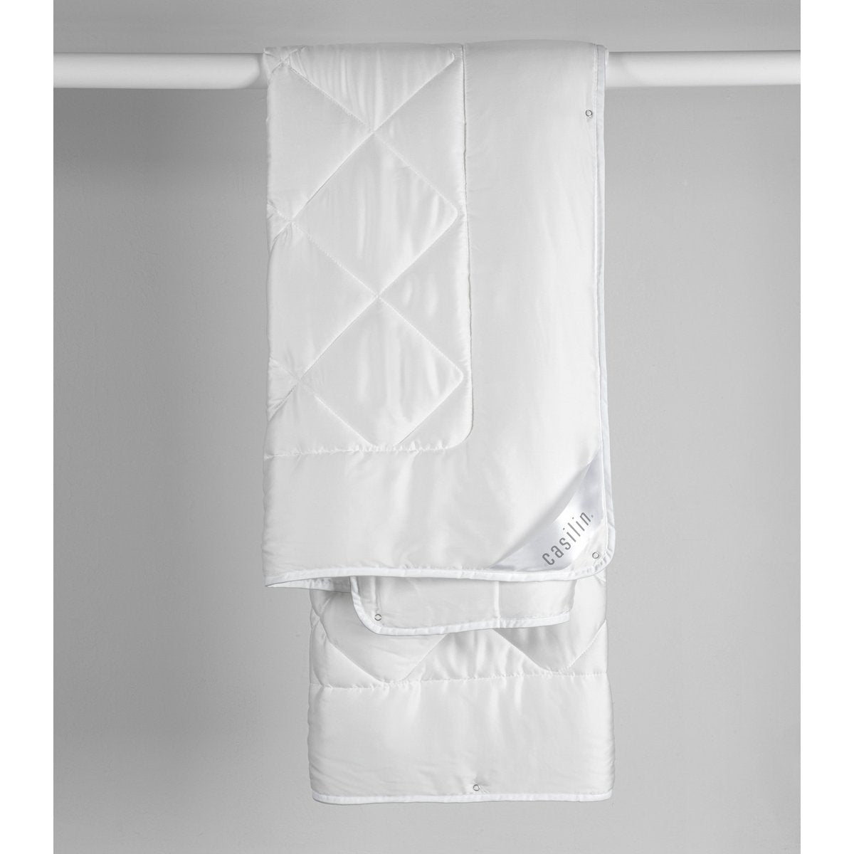 White Casilin Super Soft Duo duvet hanging folded, showing diamond-quilted Tencel satin and press-stud eyelets