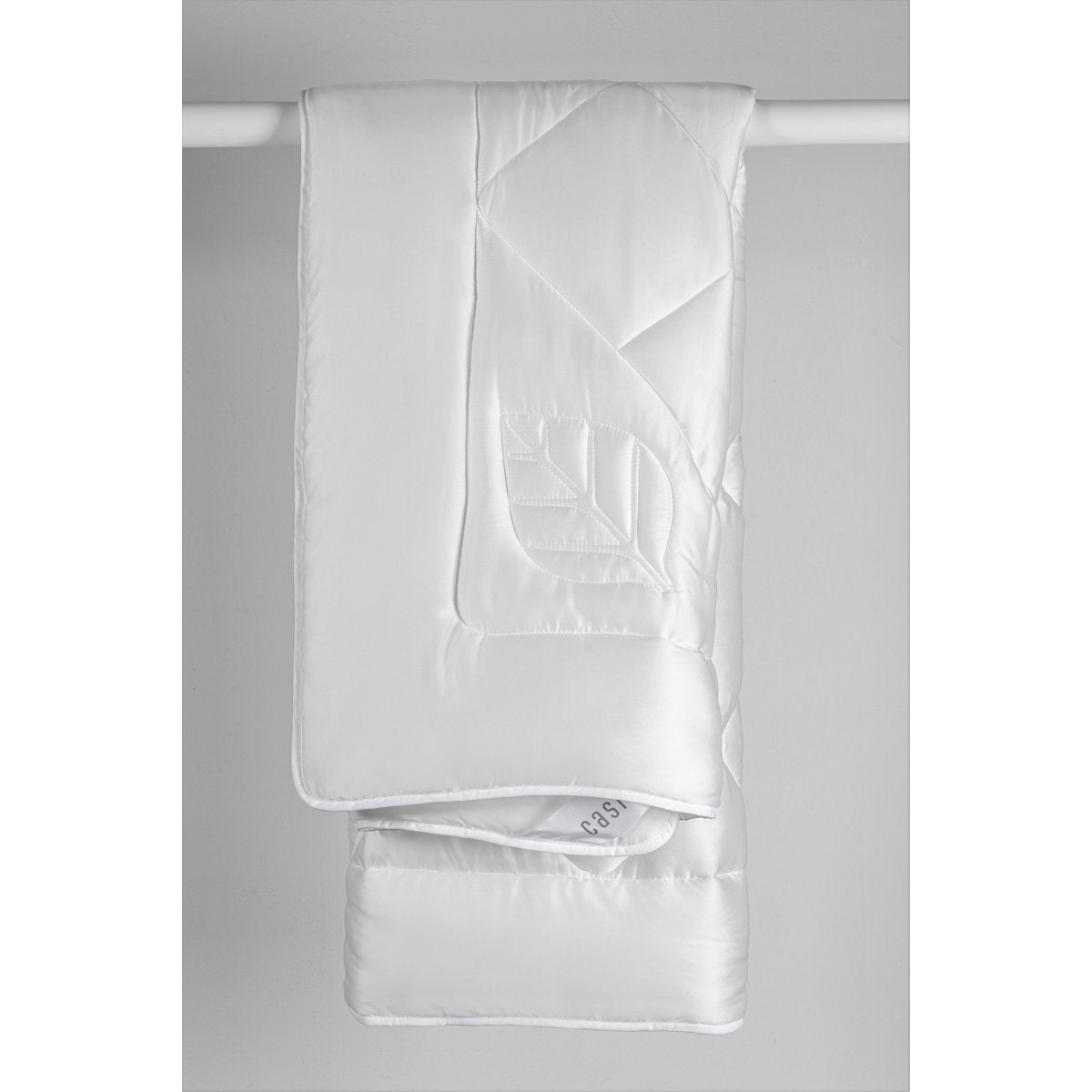 White Casilin Super Soft Mono duvet hanging folded, showing leaf-quilted Tencel satin and Casilin label