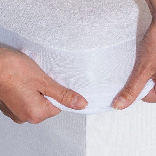 Close-up of hands lifting the elasticated corner skirt of the white terry mattress protector