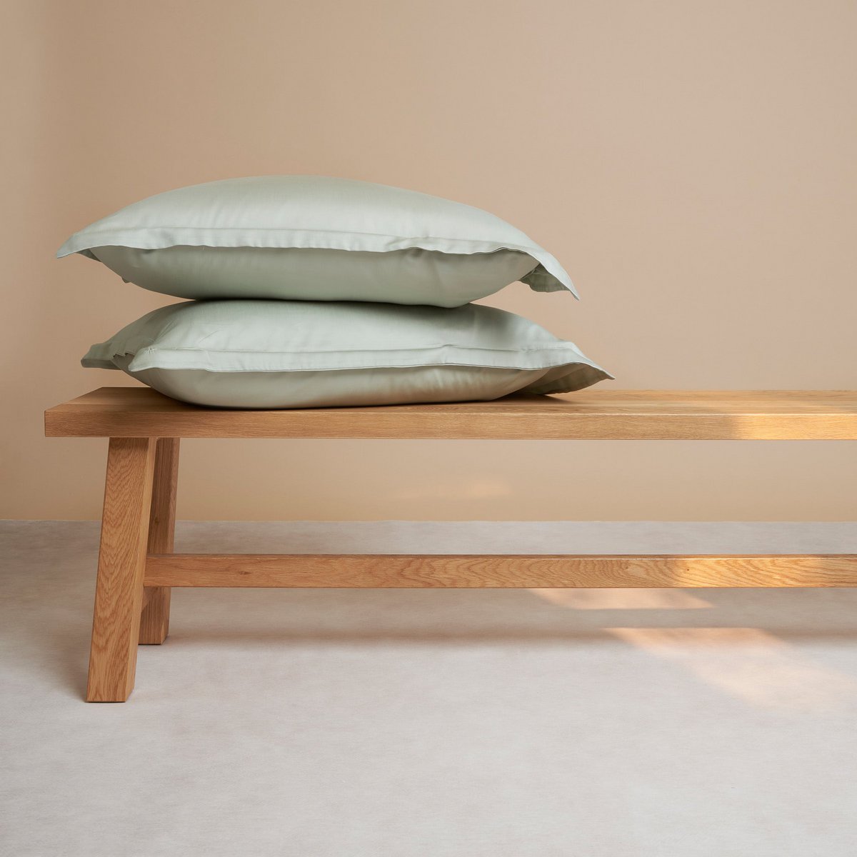 Tencel™ Sateen Pillowcases in Gray Green, stacked on a wooden bench