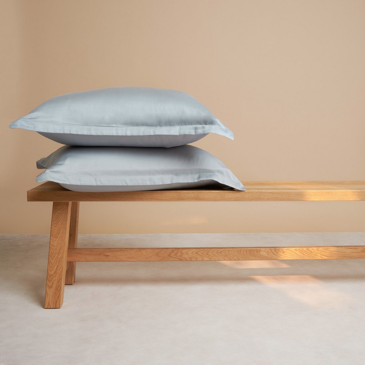 Tencel™ Sateen Pillowcases in Gray Blue, stacked on a wooden bench