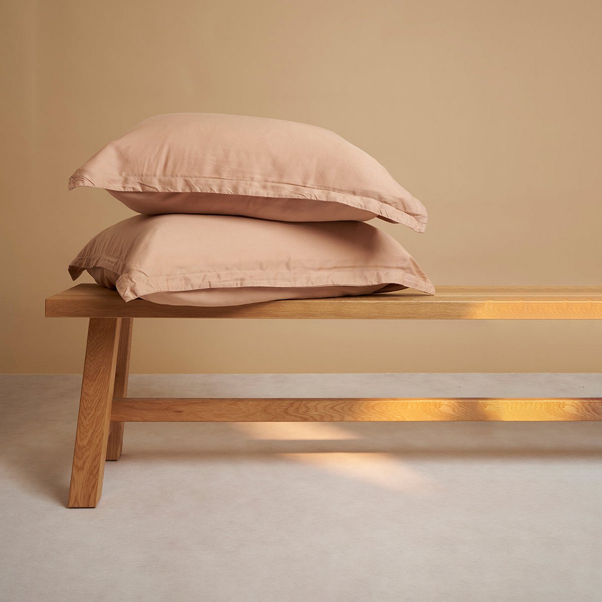 Alt text: Tencel™ Sateen Pillowcases in Peach, stacked on a wooden bench