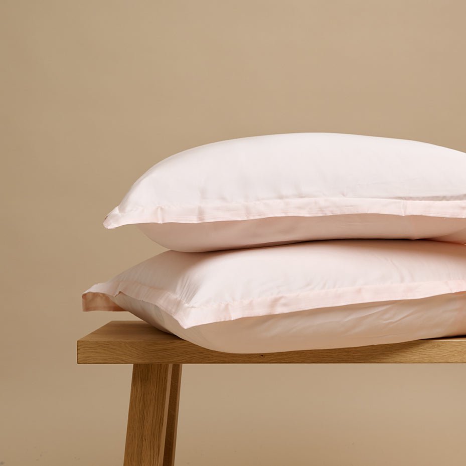 Tencel™ Sateen Pillowcase in Peach White stacked on a wooden bench