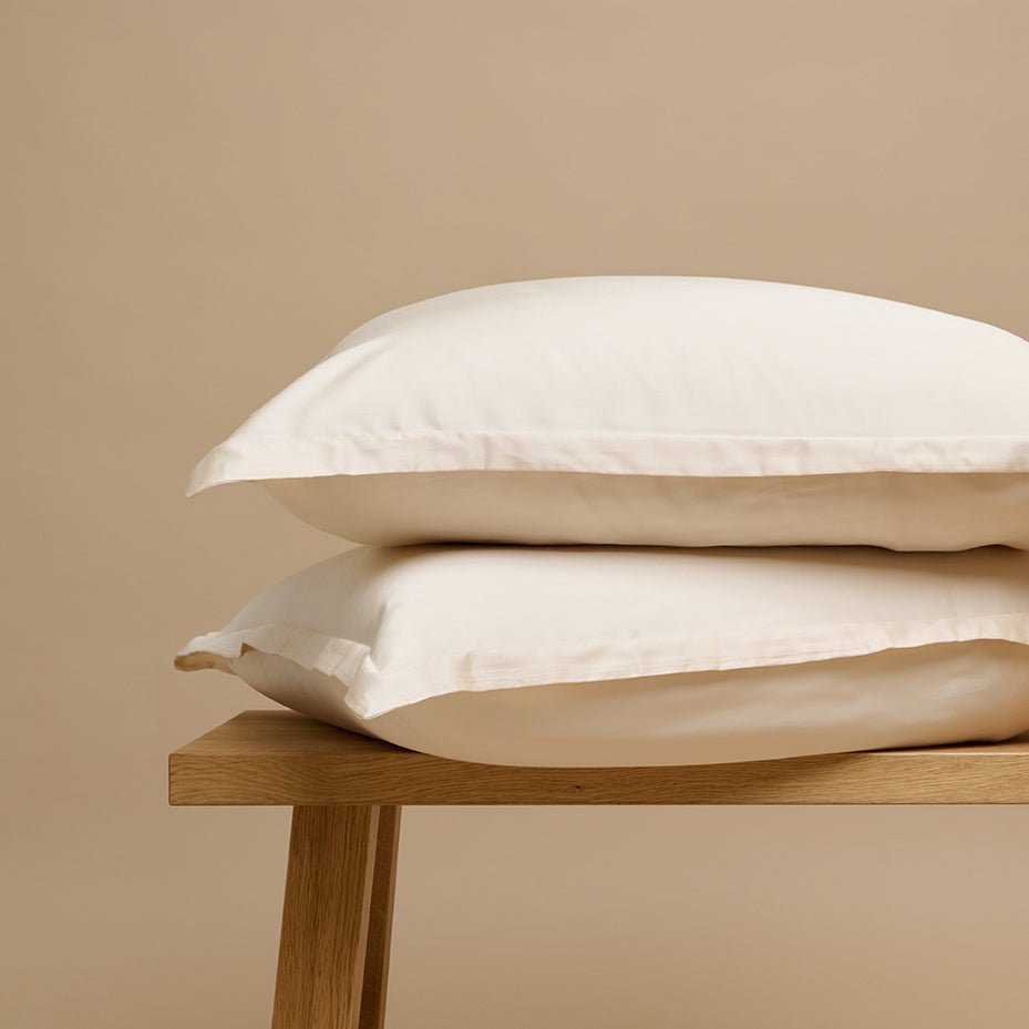 Tencel™ Sateen Pillowcase in White Sand stacked on a wooden bench