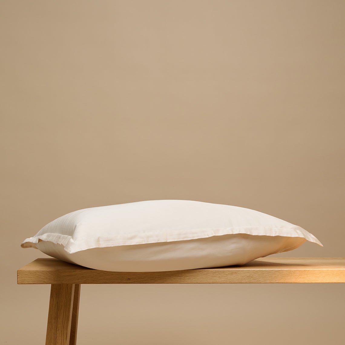 Tencel™ Sateen Pillowcase in White Sand shown from the side on a wooden bench