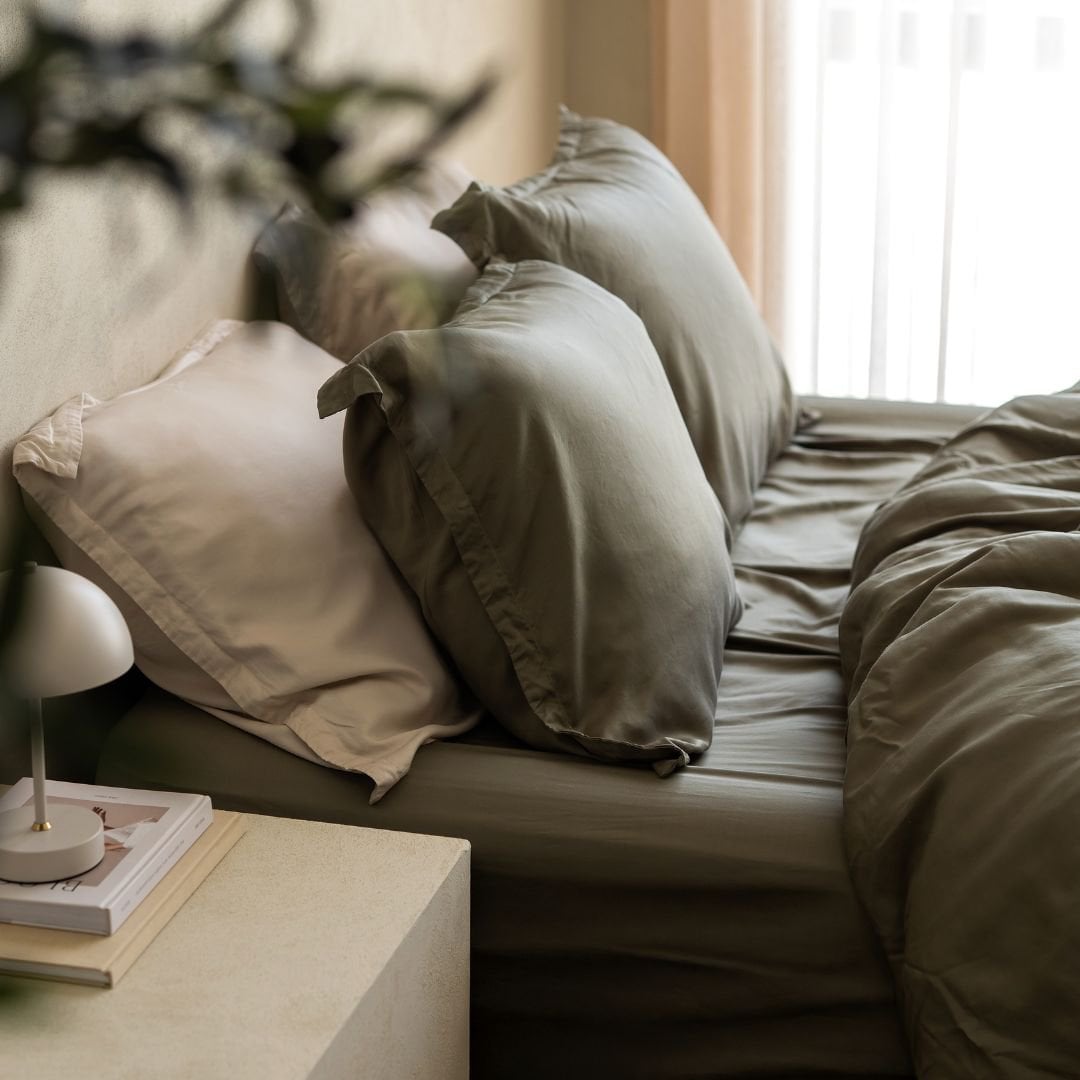 Person resting on a bed dressed in the Tencel™ Twill Duvet Cover in Olive Green