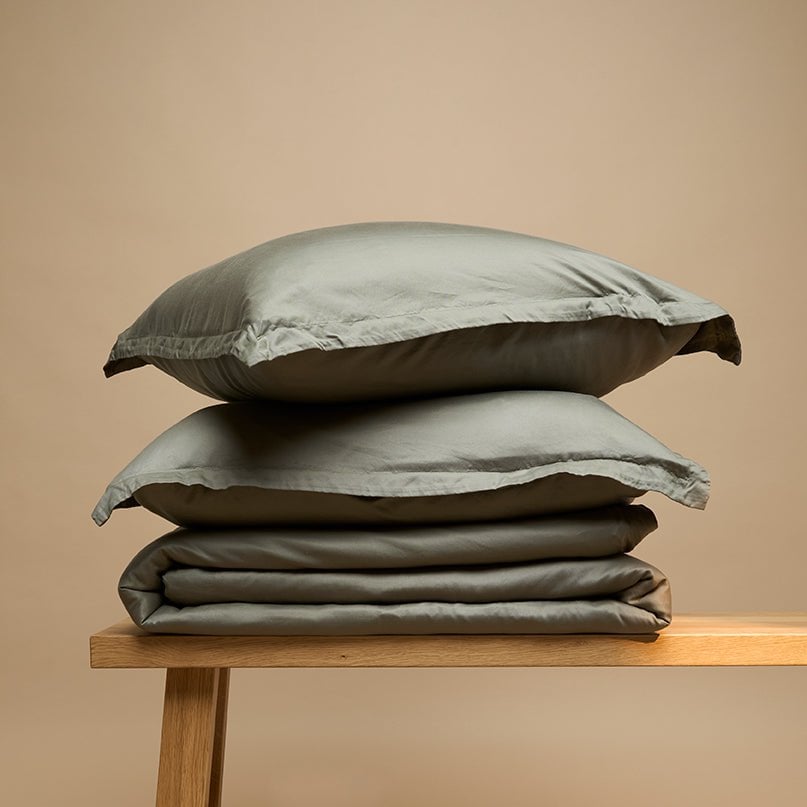Tencel™ Twill Duvet Cover and pillows in Olive Green, folded on a bench