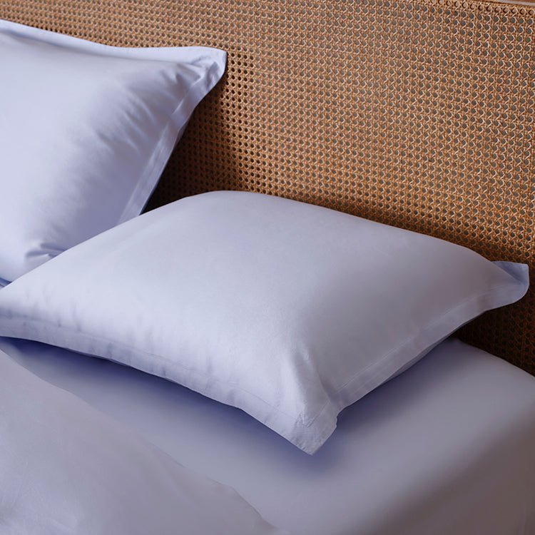 Tencel™ Twill Pillowcase in Lavender Blue styled on a bed against a rattan headboard