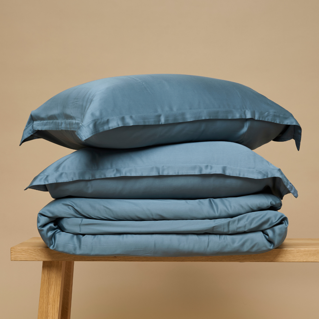 Eco Bamboo Duvet Cover and pillows in Ocean Blue, folded on a wooden bench