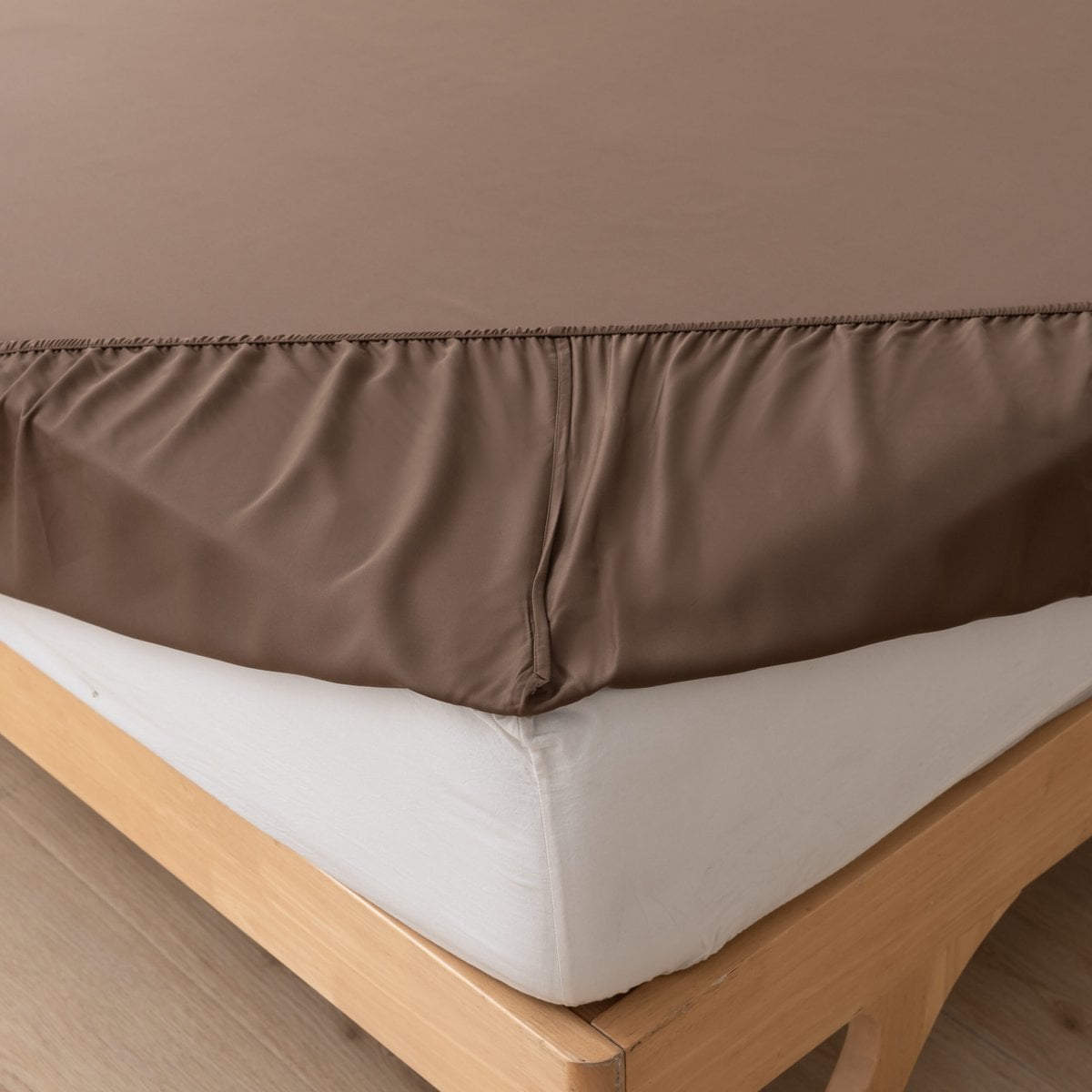 Close-up of the Coffee Brown bamboo fitted sheet's corner fitted over a mattress on a wood bed frame.