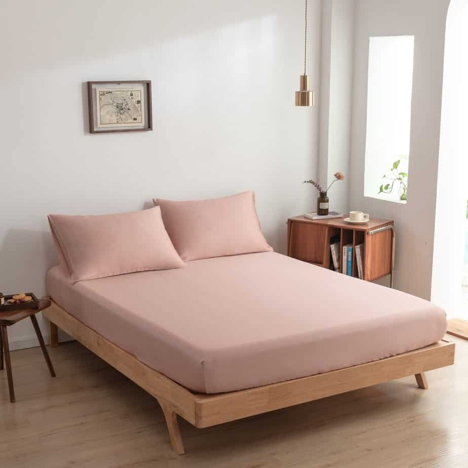 Cuddle Pink bamboo fitted sheet styled on a wood-frame bed in a bright bedroom.