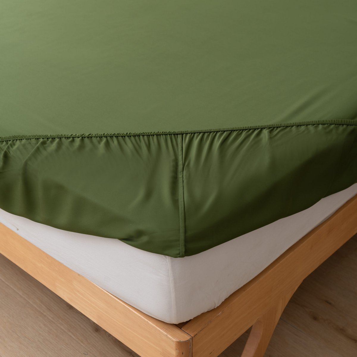 Close-up of the Deep Moss bamboo fitted sheet's elasticated corner fitted over a mattress on a wood bed frame.