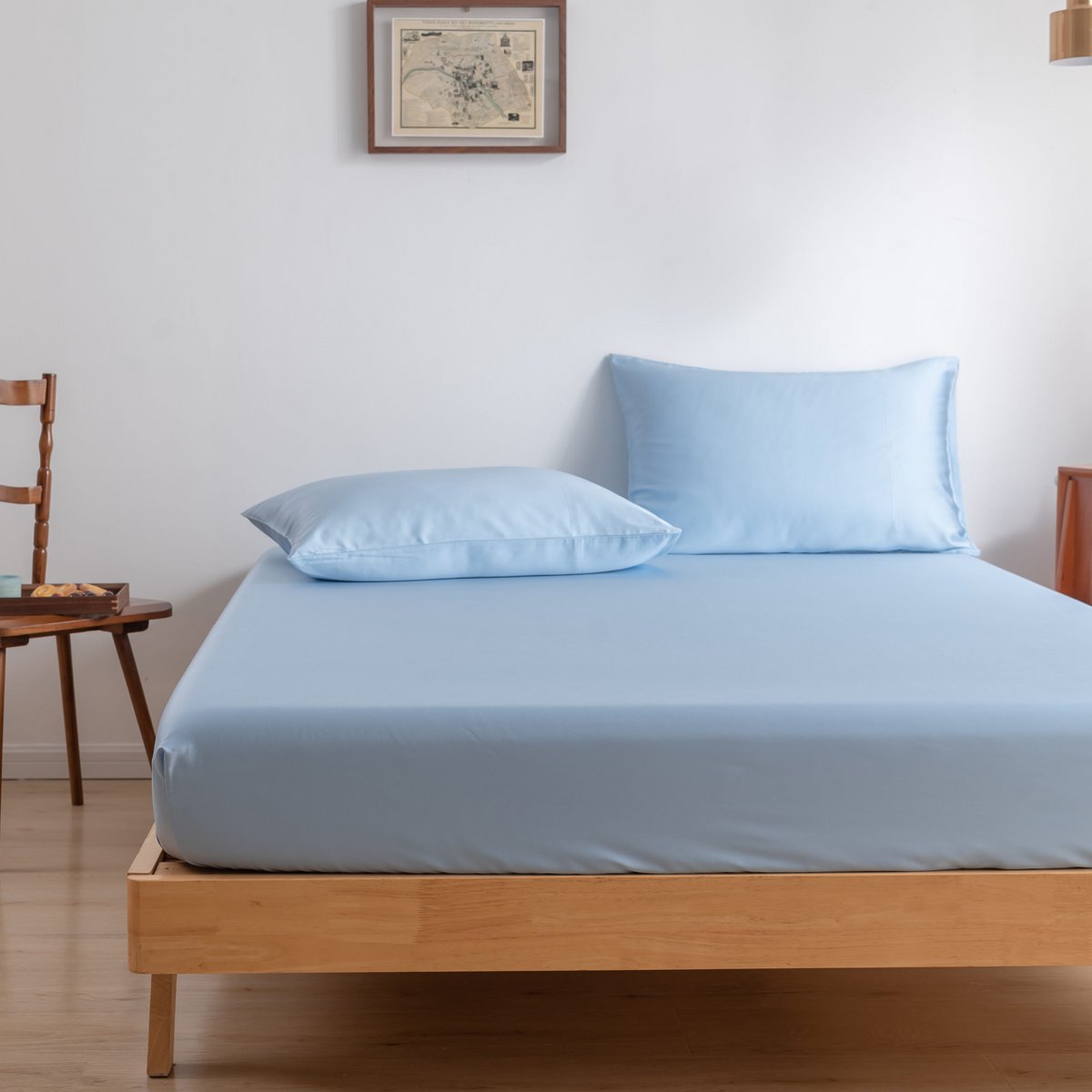 Sky Blue bamboo fitted sheet on a bed beside a wooden chair and side table.
