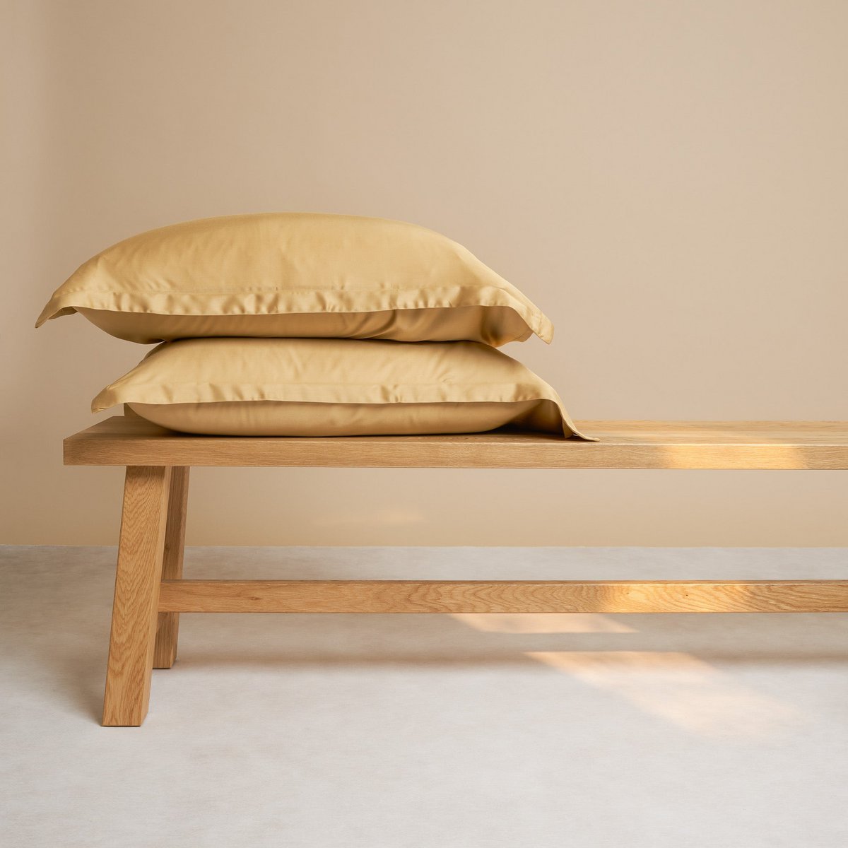 Bamboo Pillowcases in Ochre Yellow, stacked on a wooden bench