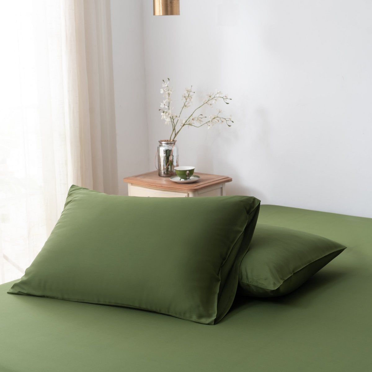 Deep Moss bamboo pillowcases styled on a bench in a bedroom setting