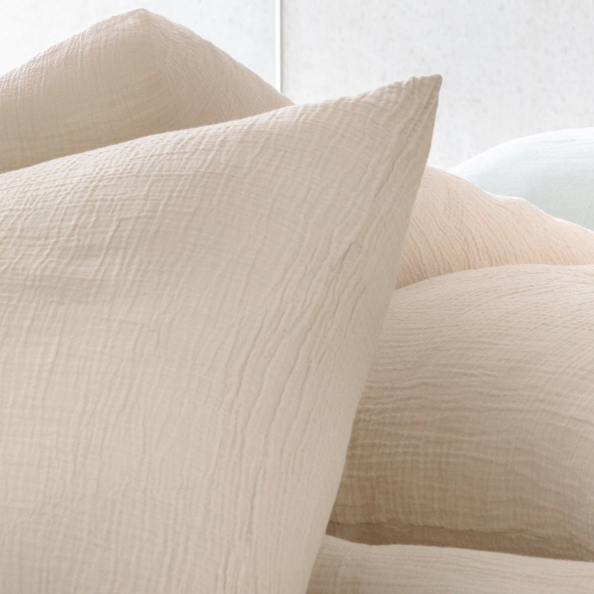 Close-up of stacked ecru cotton muslin pillowcases showing the naturally wrinkled fabric texture