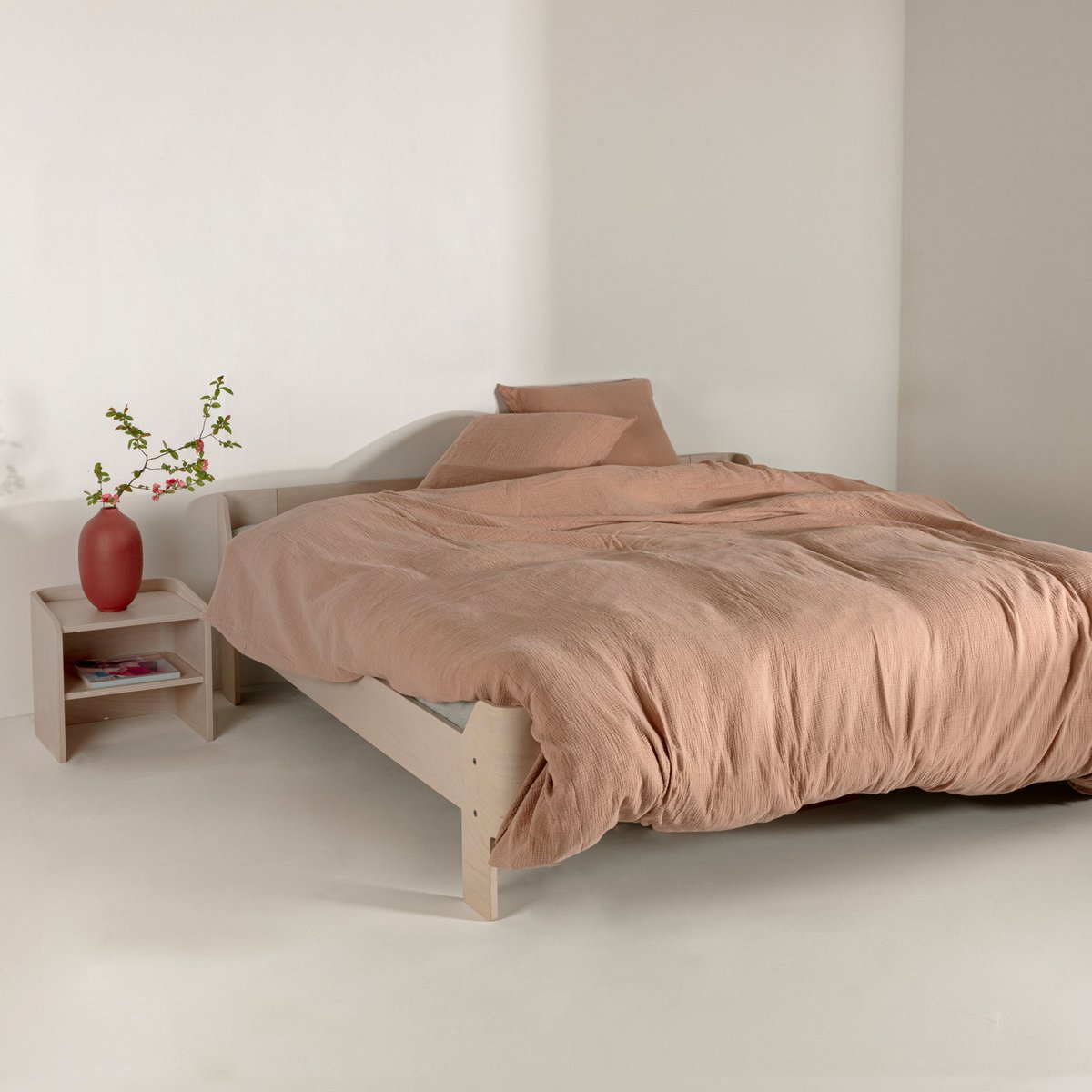 Sahara pink cotton muslin duvet cover styled on a wooden bed frame with a red vase of flowers on the nightstand