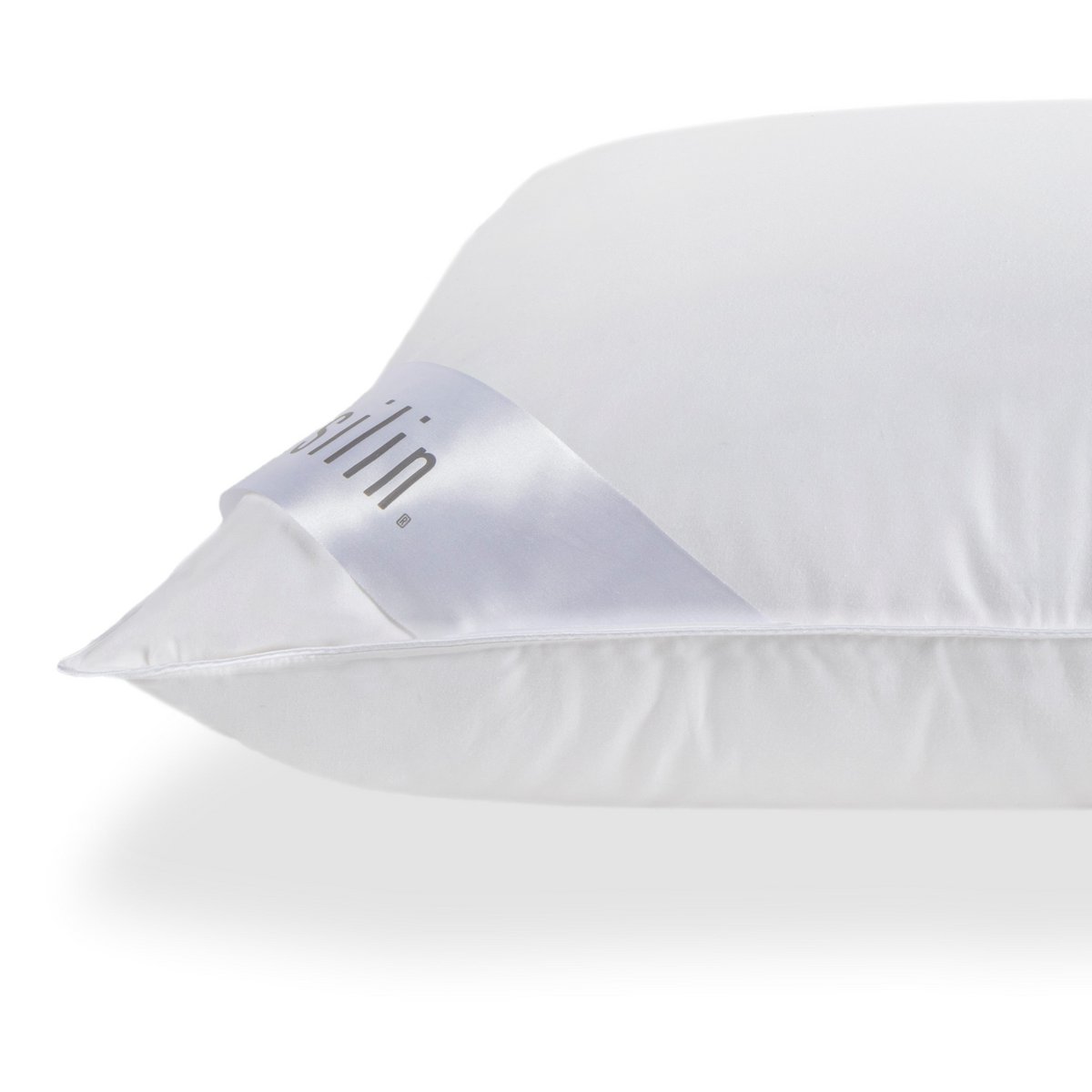 Close-up of the corner of a white Casilin down pillow showing the satin brand label and piped edge