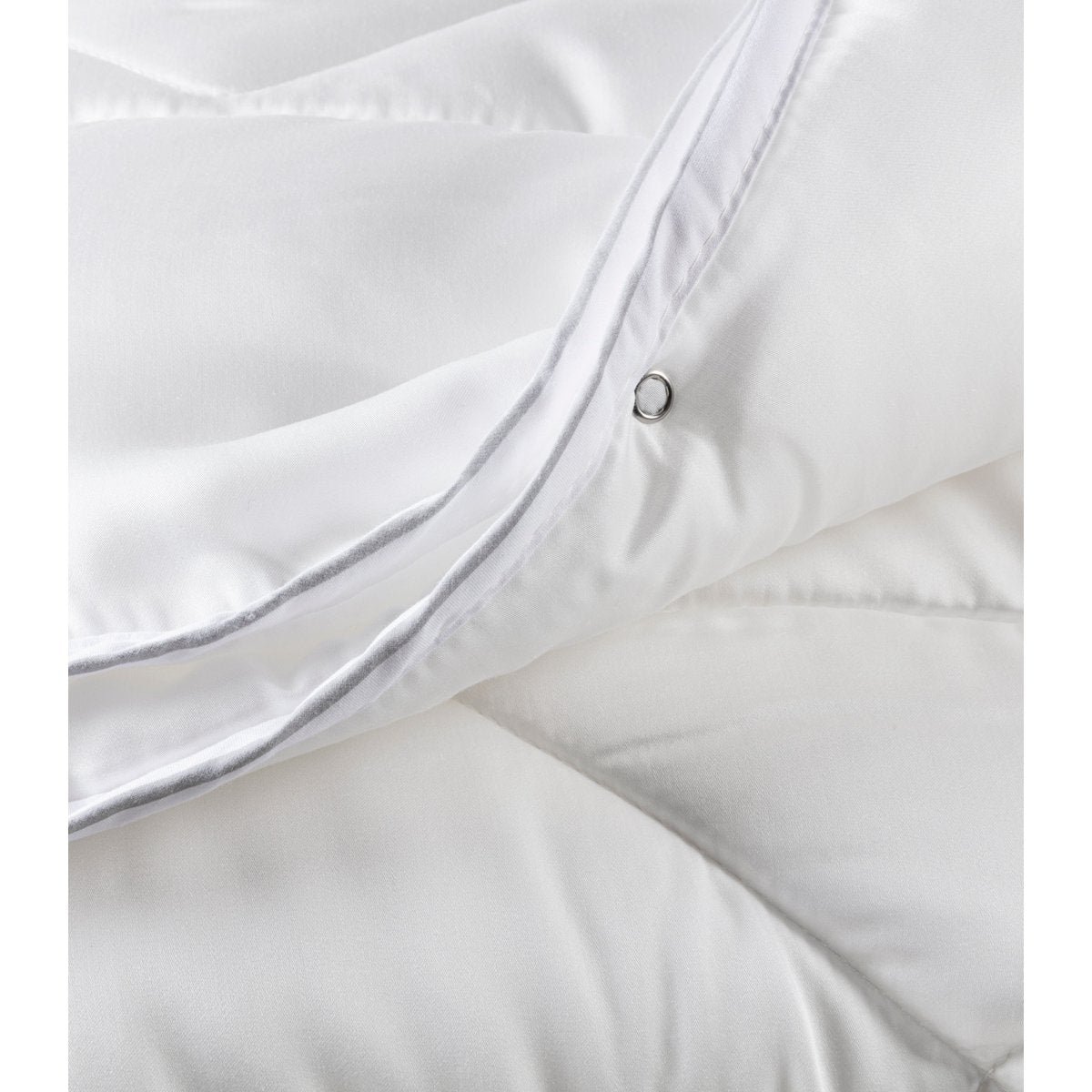 Close-up of the metal press-stud eyelet on the white cotton satin Satin Duo duvet used to connect the two layers