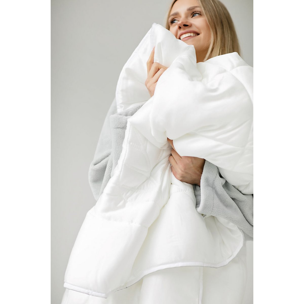 Woman in a grey robe smiling while hugging the folded white Super Soft Light duvet