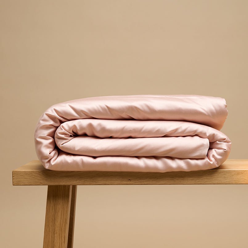 Eco Bamboo Duvet Cover in Powder Peach, folded on a wooden bench