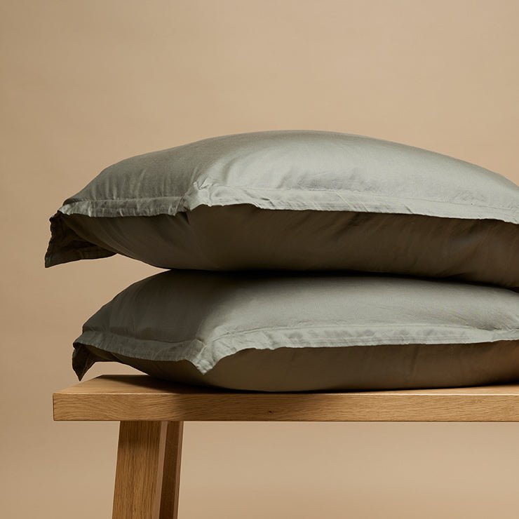 Tencel™ Sateen Pillowcases in Olive Green, stacked on a wooden bench