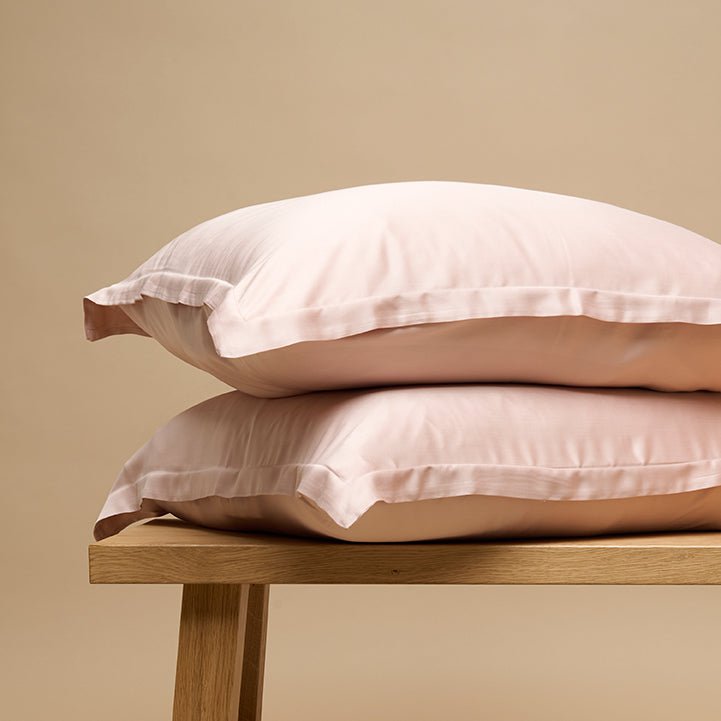 Tencel Sateen pillowcases in peach white styled on a wooden bench