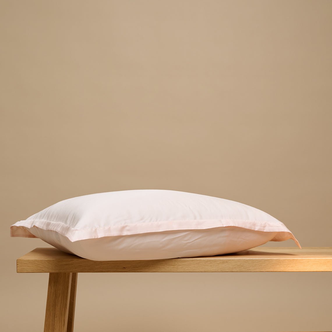 Tencel™ Sateen Pillowcase in Peach White shown from the side on a wooden bench