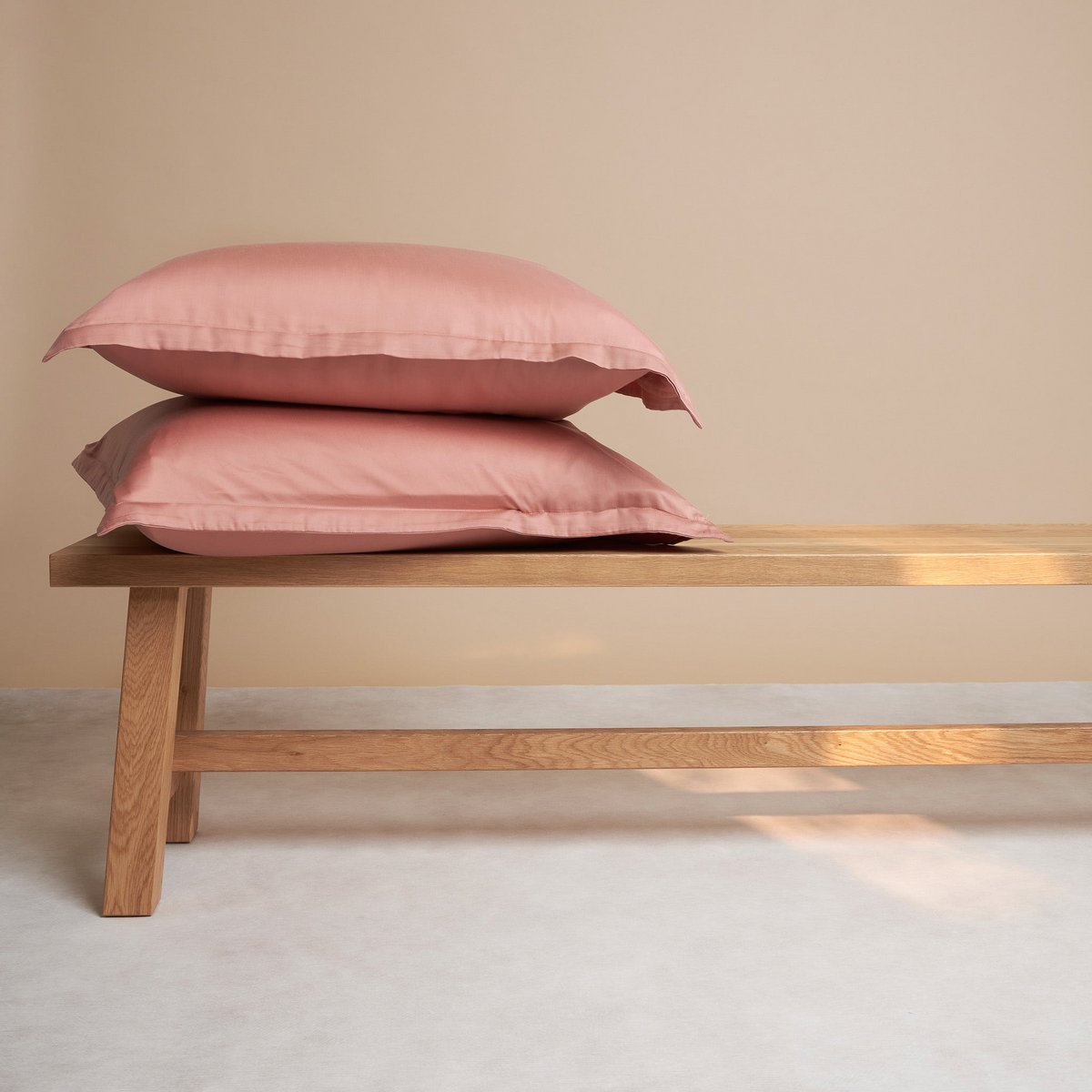 Tencel™ Sateen Pillowcases in Terra Pink, stacked on a wooden bench