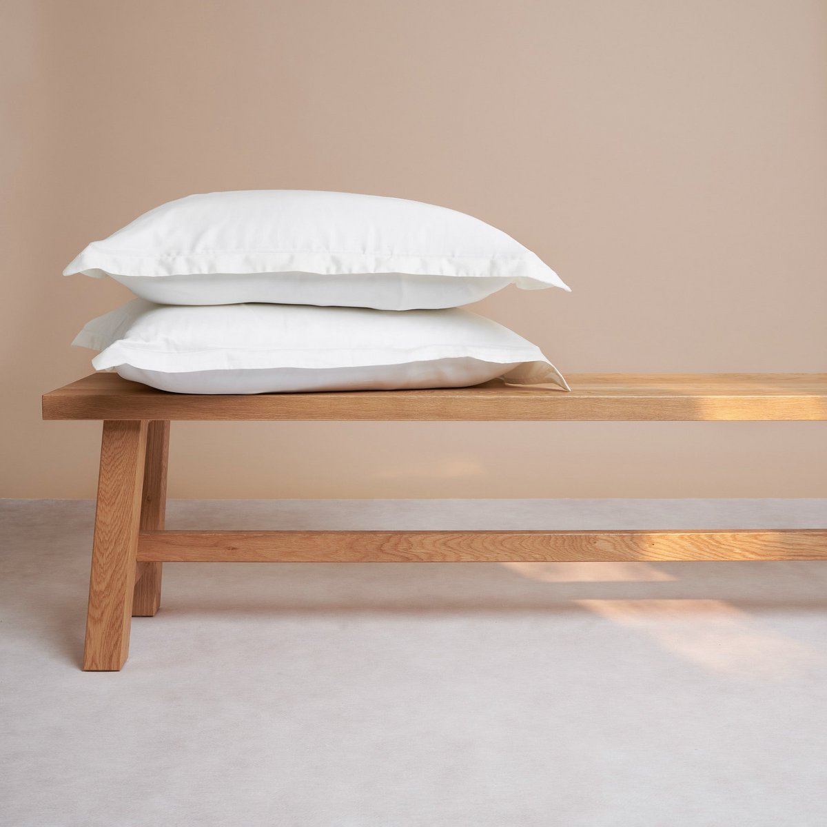 Tencel™ Sateen Pillowcase in White stacked on a wooden bench
