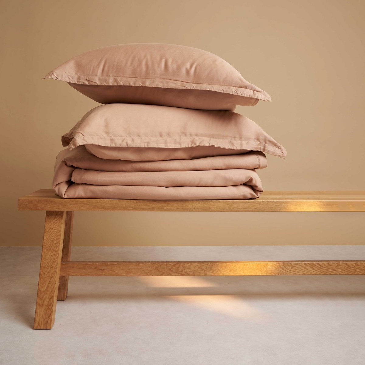 Tencel™ Twill Duvet Cover and pillows in Peach, folded on a bench