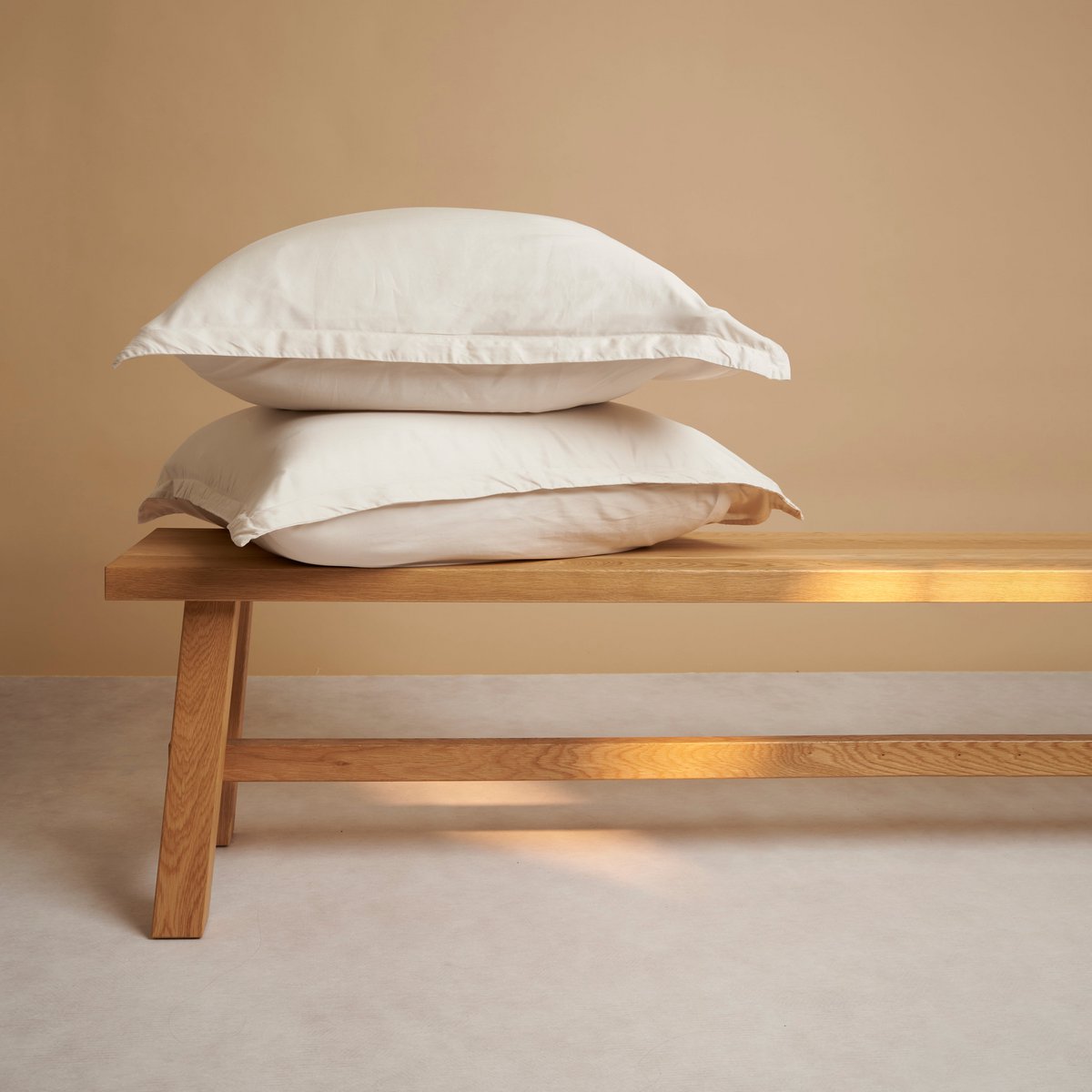 Tencel™ Twill Pillowcases in Beige, stacked on a wooden bench