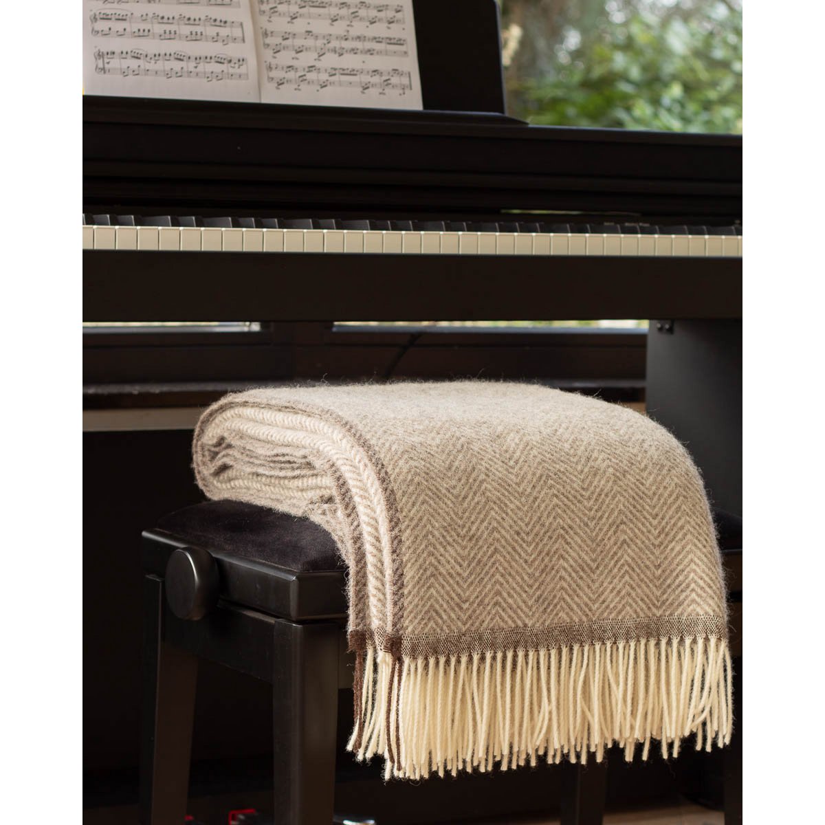 Beige blanket with fringe draped over a piano stool in front of a piano